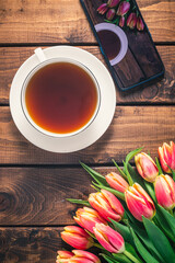 A bouquet of tulips lies on a wooden table next to a coffee mug.