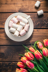 A bouquet of tulips lies on a wooden table next to a coffee mug.