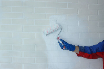 Close-up of workers' hands at builders work painting a wall in a room with a paint roller. Worker painting a brick wall white