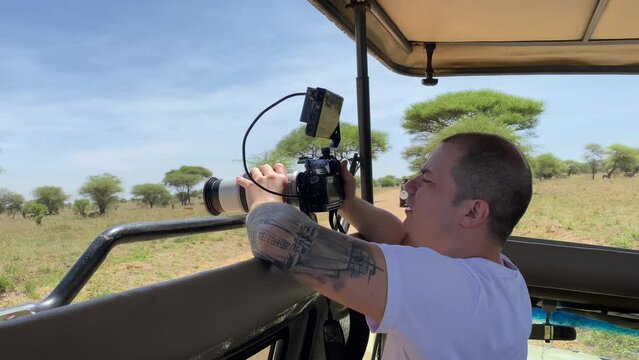 A tourist with a large camera takes pictures of animals from a safari jeep. Tarangire National Park. Safari in Tanzania, Africa.