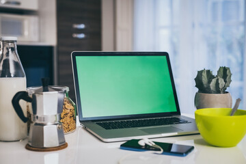 Table set for breakfast, kitchen in the background. Natural meal and technology devices. Interior view of a cozy and modern home. Millennial, youth, home working, home schooling, remote work concept.