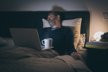 Tired man sleeping on bed after hard works with laptop until late at night. Bored boy sitting in bedroom use online devices. Smart working, home school, internet lifestyle new technology concept