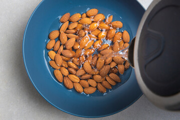 almonds in a blue bowl are poured with boiling water from a kettle on a concrete background. concept for a recipe for making almond flour. top view