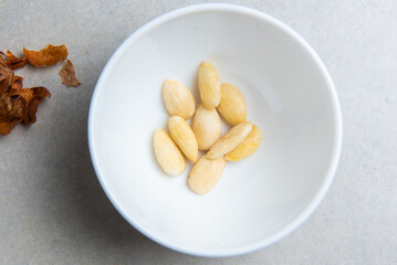 peeled almonds in a white bowl and a peel from it next to a concrete background. concept for a recipe for making almond flour. top view