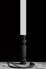 Flashlight stands on a table with a narrow beam of light upwards on a black background