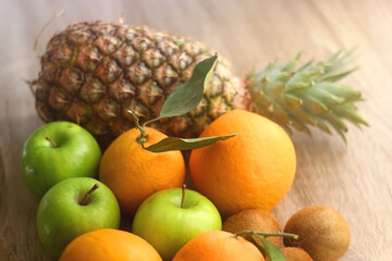 Pineapple, apples, oranges, lemons and kiwis on a wooden table. Selective focus.