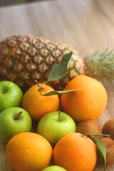 Fototapeta na wymiar Pineapple, apples, oranges, lemons and kiwis on a wooden table. Selective focus.
