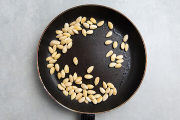 peeled almonds in a frying pan on a concrete background. concept for a recipe for making almond...