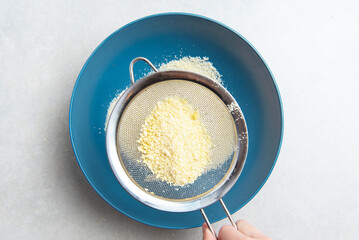 almond flour is sifted through a sieve into a blue bowl on a background of concrete. concept for a recipe for making almond flour. top view