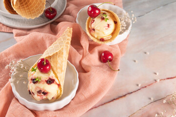 Traditional waffle cones with ice cream and cherry fruits on marble stone surface