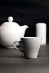 White dishes. Cup of coffee, teapot and candle on black.