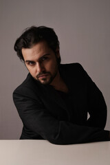 Vertical portrait of man in suit sits over white wall looking at the camera.