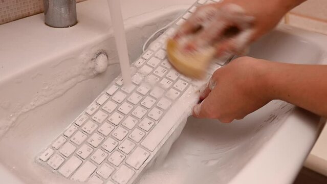 Woman washing white computer keyboard with a sponge with foam.