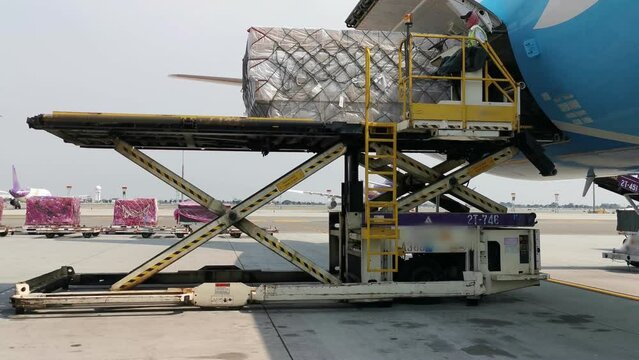 A worker is loading a cargo containers from the freighter airplane at the airport. In the logistic industry the air transport is very popular.