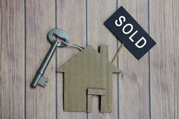 Sold text on dark paper with house model and key on wooden desk
