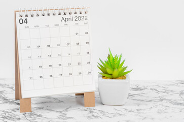 April 2022 desk calendar with plant on marble table.