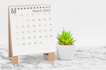 March 2022 desk calendar with plant on marble table.