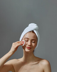 Beautiful young girl with towel on head hold cotton pad cleansing face skin remove makeup, enjoy skincare beauty routine - obrazy, fototapety, plakaty