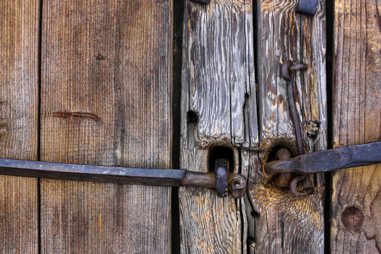 Log old house. Doors, gates. Forged rusty metal door handles, bolts, hinges, hooks. Shabby tree, aged wood structure.