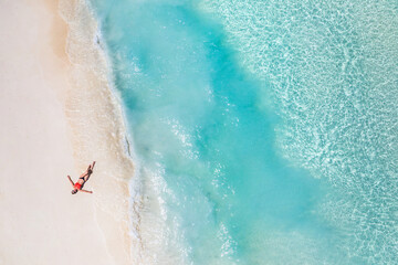 Aerial view of a woman relaxing on tropical beach Maldives islands. Vacation adventure aerial beach landscape, turquoise water, soft sand. Amazing top view from drone beach shore azure lagoon seaside - obrazy, fototapety, plakaty