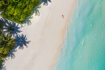 Aerial view of a woman relaxing on tropical beach Maldives islands. Vacation adventure aerial beach landscape, turquoise water, soft sand. Amazing top view from drone beach shore azure lagoon seaside