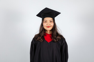 Graduate female student in mortarboard and bachelor gown on white background