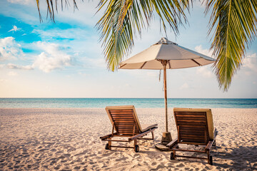 Fantastic beach scene with two sun beds loungers under umbrella and palm leaves. Tropical nature...