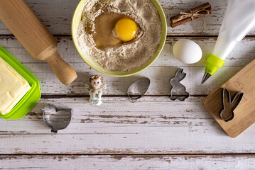 Baking ingredients for baking Easter cookies - flour, eggs, cinnamon, butter, kitchen utensils and different shapes, on a blue wooden background. View from above. copy space