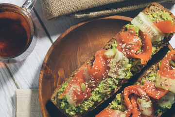 Bruschetta with salmon and avocado on a wooden plate on a white wooden background.