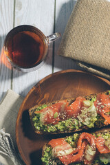 Bruschetta with salmon and avocado on a wooden plate on a white wooden background.
