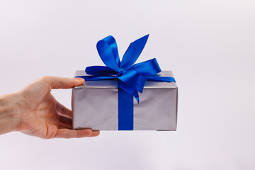 A man's hand holds a gift box with a blue ribbon on a white background. Close-up. Copy space.
