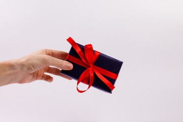 A man's hand holds a black gift box with a red ribbon on a white background. Close-up. Copy space.