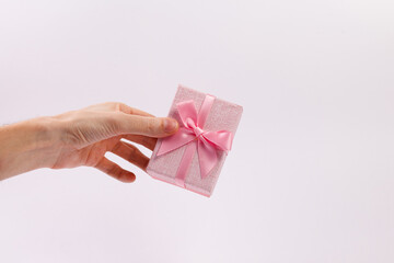 A man's hand holds a pink gift box with a pink ribbon on a white background. Close-up. Copy space.