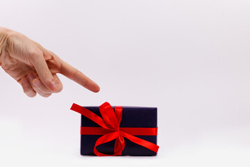 A man's hand points a finger at a black gift box with a red ribbon. Close-up. Copy space.