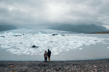 A couple at Fjallsárlón glacial lagoon, Southeast Iceland. Icebergs in lagoon, cloudy sky.