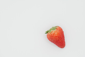A single bright red strawberry placed in a space with a pure white background.