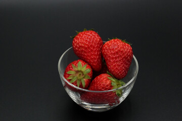 A space with a pitch-black background, lots of strawberries served in a glass bowl.