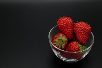 A space with a pitch-black background, lots of strawberries served in a glass bowl.