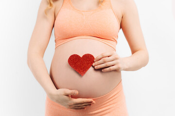 Young pregnant woman holding and touching her belly, holding a red heart sign, belly close-up