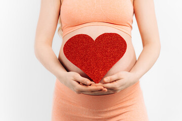 Belly of a pregnant woman and a red heart on a white background.The concept of motherhood