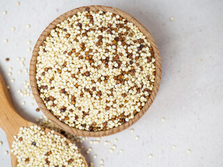 Raw mixed quinoa in bowl and scoop on light concrete background. Healthy and diet superfood