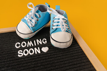 Tiny baby's shoes and a board with the inscription "coming soon". Pregnancy concept and expecting baby