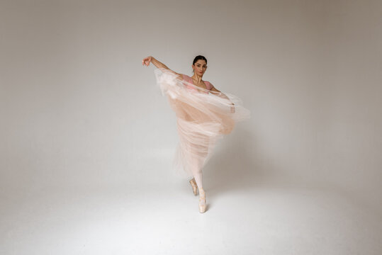 young pretty, fragile, beautiful ballerina dancing in a long pale pink dress with a tulle on a uniform background, low key. Ballet, dancing, dancer