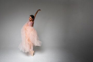 Fototapeta premium young pretty, fragile, beautiful ballerina dancing in a long pale pink dress with a tulle on a uniform background, low key. Ballet, dancing, dancer