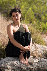 Fototapeta na wymiar Vertical shot of a beautiful female Latina sitting on a rock by the bush