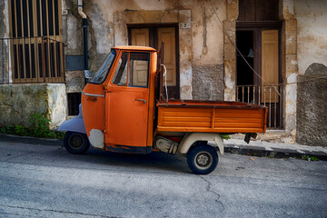 Ape, light three-wheeled vehicle.ape open backed van parked it Italian piazza.Ape, three-wheeled light commercial vehicle. Italy.