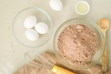 Cocoa  flour, eggs, oil, wooden spoon, kitchen towel on a kitchen top 