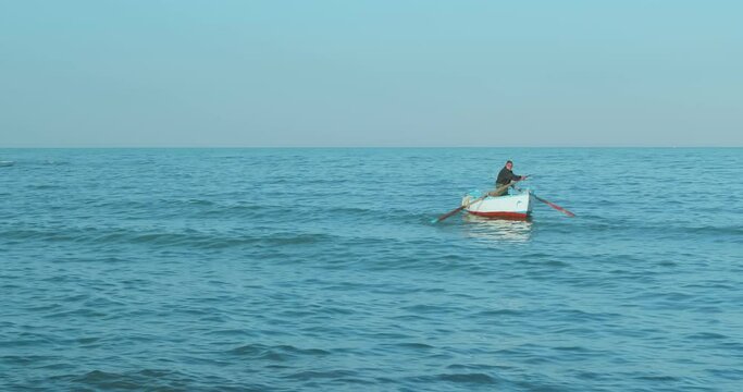 Old fisherman spreads his fishing nets in the sea, near the shore, on board a small and characteristic fishing boat (called gozzo in Puglia)