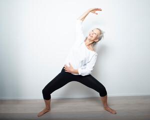 bellissima donna felice  over 50 con i capelli bianchi che fa yoga su sfondo chiaro 