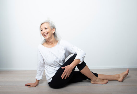 bellissima donna felice  over 50 con i capelli bianchi che fa yoga su sfondo chiaro 